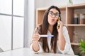 Young brunette woman holding pregnancy test result speaking on the phone looking at the camera blowing a kiss being lovely and