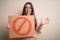 Young brunette woman holding protest banner with prohibited symbol over isolated background very happy and excited, winner