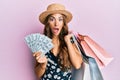 Young brunette woman holding shopping bags and dollars afraid and shocked with surprise and amazed expression, fear and excited Royalty Free Stock Photo