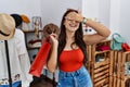 Young brunette woman holding shopping bags at retail shop smiling and laughing with hand on face covering eyes for surprise