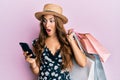 Young brunette woman holding shopping bags and smartphone afraid and shocked with surprise and amazed expression, fear and excited Royalty Free Stock Photo