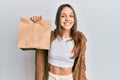 Young brunette woman holding take away paper bag looking positive and happy standing and smiling with a confident smile showing Royalty Free Stock Photo