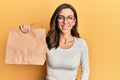 Young brunette woman holding take away paper bag looking positive and happy standing and smiling with a confident smile showing Royalty Free Stock Photo