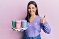 Young brunette woman holding tray with take away coffee smiling happy and positive, thumb up doing excellent and approval sign Royalty Free Stock Photo