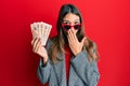 Young brunette woman holding united kingdom 10 pounds banknotes covering mouth with hand, shocked and afraid for mistake