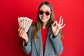 Young brunette woman holding united kingdom 10 pounds banknotes doing ok sign with fingers, smiling friendly gesturing excellent