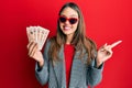 Young brunette woman holding united kingdom 10 pounds banknotes smiling happy pointing with hand and finger to the side