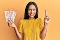 Young brunette woman holding 10 united kingdom pounds banknotes smiling with an idea or question pointing finger with happy face,