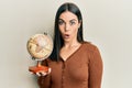 Young brunette woman holding vintage world ball scared and amazed with open mouth for surprise, disbelief face Royalty Free Stock Photo