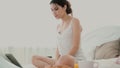 Young brunette woman at home stretches on a bed. Beautiful girl using laptop to connect during breakfast. Royalty Free Stock Photo