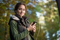 Young brunette woman listening to music in autumn park.