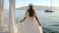 Young brunette woman with long hair wearing hat and long white dress running on the wooden pier in the sea lit by sunset Royalty Free Stock Photo