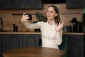 A young brunette woman makes a video call from her smartphone while sitting in the kitchen at home Royalty Free Stock Photo