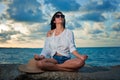 Young brunette woman meditating by the ocean at sunset Royalty Free Stock Photo