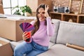 Young brunette woman moving to a new home choosing wall painting smiling happy doing ok sign with hand on eye looking through Royalty Free Stock Photo