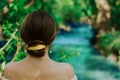 Young brunette woman with naked shoulders and elegant twist hairstyle with golden hairpin enjoys trees and river side back shot Royalty Free Stock Photo