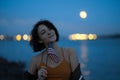 American flag: Young brunette woman at night at a place where river meets the sea in port - Visible full moon Royalty Free Stock Photo