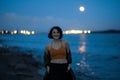 Young brunette woman at night at a place where river meets the sea in port - Visible full moon Royalty Free Stock Photo