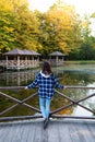 A young brunette woman in a plaid shirt stands with her back near the pond and enjoys the autumn warm day Royalty Free Stock Photo