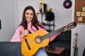 Young brunette woman playing classic guitar at music studio smiling happy and positive, thumb up doing excellent and approval sign Royalty Free Stock Photo