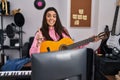 Young brunette woman playing classic guitar at music studio smiling with an idea or question pointing finger with happy face, Royalty Free Stock Photo