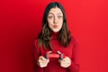 Young brunette woman playing video game holding controller puffing cheeks with funny face Royalty Free Stock Photo