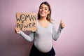 Young brunette woman pregnant expecting baby holding banner asking for women power happy with big smile doing ok sign, thumb up