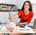 Young brunette woman putting euro coin in piggy bank saving for travel looking positive and happy standing and smiling with a Royalty Free Stock Photo