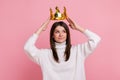 Young brunette woman putting on golden crown, looking with arrogance and smile, privileged status.