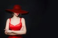 Young brunette woman with red lips makeup and diamond necklace and earrings and in burgundy wide hat, portrait on black background Royalty Free Stock Photo