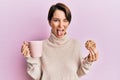 Young brunette woman with short hair drinking a cup of coffee and cookie sticking tongue out happy with funny expression Royalty Free Stock Photo