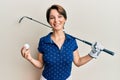 Young brunette woman with short hair holding ball and golf club smiling with a happy and cool smile on face Royalty Free Stock Photo