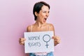 Young brunette woman with short hair holding woman rights banner angry and mad screaming frustrated and furious, shouting with