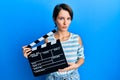 Young brunette woman with short hair holding video film clapboard clueless and confused expression