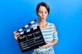 Young brunette woman with short hair holding video film clapboard making fish face with mouth and squinting eyes, crazy and Royalty Free Stock Photo