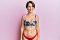 Young brunette woman with short hair wearing bikini showing tattoos looking positive and happy standing and smiling with a Royalty Free Stock Photo