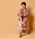 Young brunette woman with short haircut in sexy pink shiny evening costume barefoot sitting on wooden stool Royalty Free Stock Photo