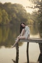 A young woman sits on the bridge by the water. Nymph girl at the lake.