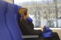 A young brunette woman sits and looks out the train window at the cityscapes. Holding a blue handbag. A blue scarf and Royalty Free Stock Photo