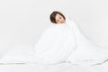 Young brunette woman sitting in bed with white sheet, pillow, wrapping in blanket on white background. Beauty female