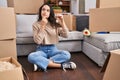 Young brunette woman sitting on the floor at new home holding keys serious face thinking about question with hand on chin, Royalty Free Stock Photo