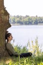 Young brunette woman sitting in green forest enjoys the silence and beauty of nature watching over a blue forest lake on Royalty Free Stock Photo