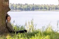 Young brunette woman sitting in green forest enjoys the silence and beauty of nature watching over a blue forest lake on Royalty Free Stock Photo