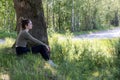 Young brunette woman sitting in green forest enjoys the silence and beauty of nature watching over a blue forest lake on Royalty Free Stock Photo