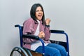 Young brunette woman sitting on wheelchair celebrating surprised and amazed for success with arms raised and eyes closed