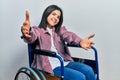 Young brunette woman sitting on wheelchair looking at the camera smiling with open arms for hug Royalty Free Stock Photo