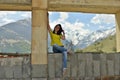 Young woman sitting on the window sill of a destroyed abandoned building in the mountains.