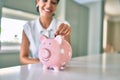 Young brunette woman smiling happy putting money savings inside of piggy bank Royalty Free Stock Photo