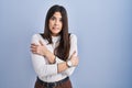 Young brunette woman standing over blue background shaking and freezing for winter cold with sad and shock expression on face Royalty Free Stock Photo