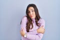 Young brunette woman standing over blue background shaking and freezing for winter cold with sad and shock expression on face Royalty Free Stock Photo